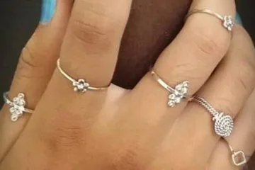 A hand displaying a set of multiple ultra-thin, stackable 925 sterling silver rings with small minimalist charms including tiny five-petal flowers, geometric dot arrangements, and a twisted silver rope design.