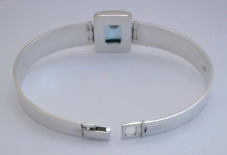 Rear open view of the modern geometric 925 sterling silver bangle displaying the back of the emerald-cut blue topaz setting and the secure interior box clasp.