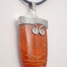 A close-up view of an artisan-crafted pendant featuring an oval-shaped orange fossil coral stone set in 925 sterling silver, accented with delicate wire-wrapped scroll details on a black cord.