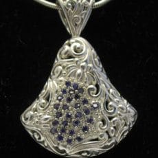 Handcrafted 925 sterling silver fan-shaped pendant featuring intricate Balinese scrollwork relief, an ornate filigree bail, and a central pave-set cluster of deep blue sapphire gemstones.