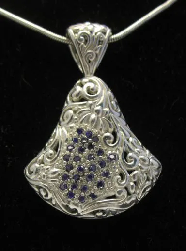 Handcrafted 925 sterling silver fan-shaped pendant featuring intricate Balinese scrollwork relief, an ornate filigree bail, and a central pave-set cluster of deep blue sapphire gemstones.