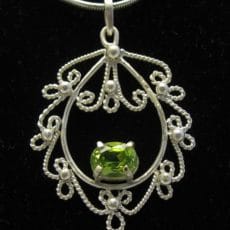Front view of an artisan-crafted 925 sterling silver filigree pendant with twisted wire scrollwork, silver granulation beads, and a prong-set oval peridot gemstone.