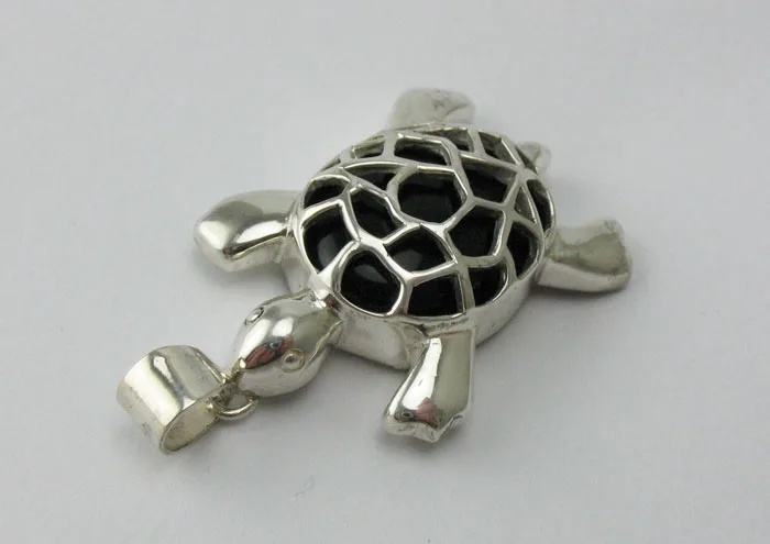 Angled view of a Balinese-style sterling silver turtle pendant showcasing the detailed openwork silver shell and polished black onyx stone inside.