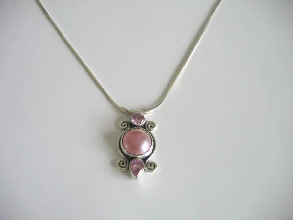 Front view of a handcrafted 925 sterling silver pendant necklace featuring a central pink cabochon framed by Balinese scrollwork and faceted pink gemstones on a sleek silver chain.