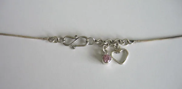 Detail view of the 925 sterling silver chain closure featuring an S-hook clasp decorated with a faceted pink gemstone charm and an open heart dangle.