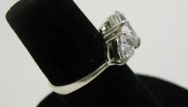 Side perspective profile view of the artisan 925 sterling silver three-stone ring displaying the raised claw prong baskets holding pear-cut clear zircons on a slender polished band.