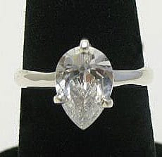 A front view of an artisan-crafted 925 sterling silver solitaire ring featuring a large, faceted pear-cut clear quartz gemstone securely held by a prong setting on a polished band, displayed on a black velvet ring cone.