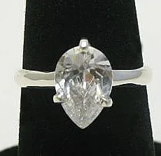 A front view of an artisan-crafted 925 sterling silver solitaire ring featuring a large, faceted pear-cut clear quartz gemstone securely held by a prong setting on a polished band, displayed on a black velvet ring cone.