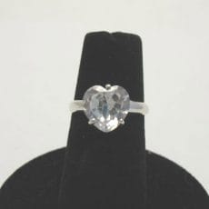 A front view of an artisan-crafted 925 sterling silver solitaire ring featuring a faceted heart-cut clear quartz gemstone held securely by a prong setting on a polished band, displayed on a black velvet ring cone.