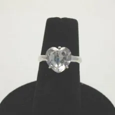 A front view of an artisan-crafted 925 sterling silver solitaire ring featuring a faceted heart-cut clear quartz gemstone held securely by a prong setting on a polished band, displayed on a black velvet ring cone.