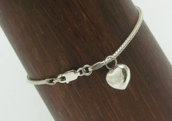 A detailed view of a sterling silver heart charm bracelet showcasing the secure lobster claw lock mechanism and the fine intricate weave of the chain.
