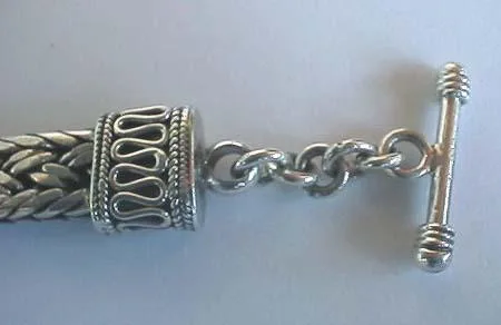 Detailed view of the handcrafted sterling silver toggle ring clasp attached to an ornate end cap featuring S-scroll filigree wirework and rope borders.