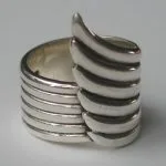 A close-up side view of a sculptural 925 sterling silver ring featuring a layered angel wing design with smooth, polished bands, captured in an artisan-crafted style against a neutral background.