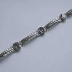 Full length view of a handcrafted 925 sterling silver link bracelet featuring oval faceted purple amethyst gemstones in rope-bordered bezels connected by sculpted feather motif links with a box clasp.