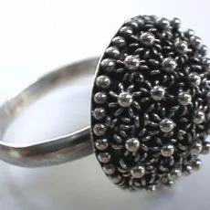 A close-up side perspective of an artisan-crafted 925 sterling silver dome ring featuring a raised cluster face decorated with traditional Balinese granulation beadwork patterns over an oxidized background on a polished silver band.