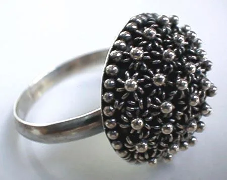A close-up side perspective of an artisan-crafted 925 sterling silver dome ring featuring a raised cluster face decorated with traditional Balinese granulation beadwork patterns over an oxidized background on a polished silver band.