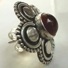 Angled view of a handcrafted 925 sterling silver stud earring featuring a rich reddish cabochon carnelian stone framed by a Balinese floral petal halo with beaded granulation and oxidized contrast.