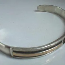 Artisan-crafted 925 sterling silver open cuff torque bangle showcasing a flat smooth band inlaid with a contrasting warm brass-toned central metallic channel, captured from an elevated three-quarter angle.