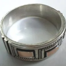 Artisan-crafted 925 sterling silver wide band ring featuring a geometric paneled motif accented with contrasting copper-tone metal rectangles and detailed Balinese rope borders, captured from a slightly elevated three-quarter view.