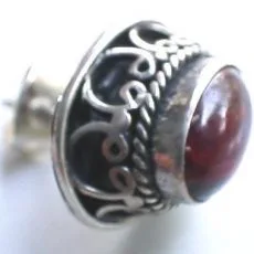 Side-profile view of a handcrafted 925 sterling silver stud earring featuring a smooth deep red garnet cabochon set in an ornate Balinese scrollwork cup with twisted rope wire trim.