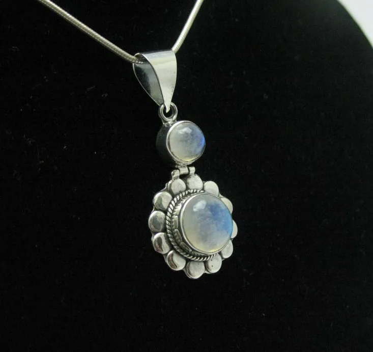 Angled studio profile shot of a handcrafted 925 sterling silver two-tier drop pendant holding two round rainbow moonstone cabochons displaying a luminous blue flash.