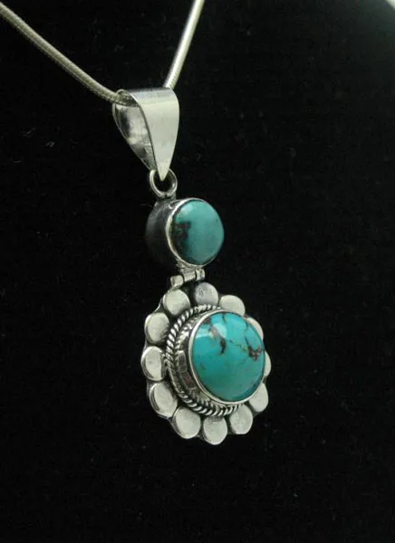 Three-quarter perspective view of an artisan-crafted sterling silver two-tier pendant featuring two genuine turquoise stones on a fine snake chain.
