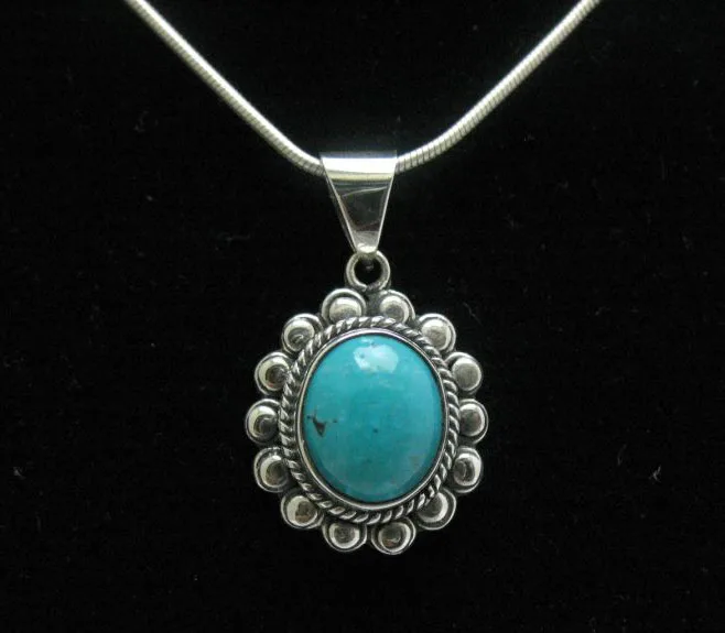 Centered close-up of a handcrafted sterling silver sunburst pendant holding an oval turquoise gemstone framed by ornate silver beads.
