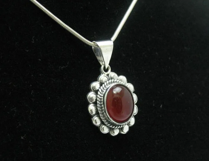 Angled view of an artisan-crafted 925 sterling silver pendant showcasing a deep red oval carnelian cabochon on a fine silver chain.