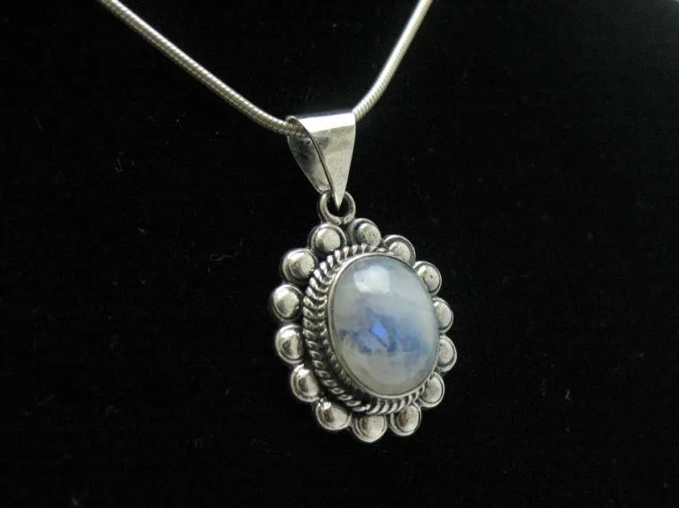 Three-quarter view of a sterling silver pendant highlighting a luminous rainbow moonstone cabochon showing a brilliant blue flash.