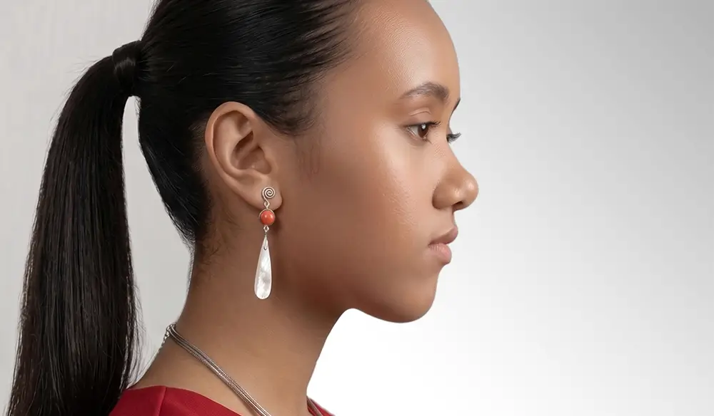 Side profile of a Balinese model wearing handmade silver Binar Silver earrings featuring a red bead and a teardrop-shaped hanger